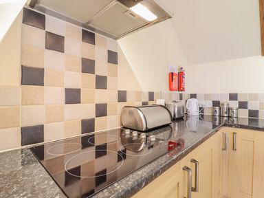 A kitchen countertop with an electric stovetop a bread box a toaster a kettle and storage canisters at Hayloft Cottage in Little Glemham near Wickham Market