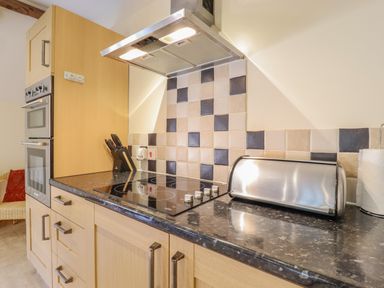 A kitchen with wooden cabinets an electric stove a knife block a stainless steel bread box and a paper towel holder at Hayloft Cottage in Little Glemham near Wickham Market