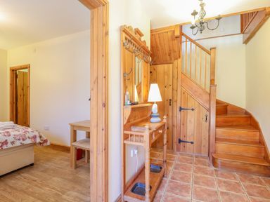 A hallway with wooden stairs a wooden coat rack with a lamp and a small table next to a bedroom at Hayloft Cottage in Little Glemham near Wickham Market