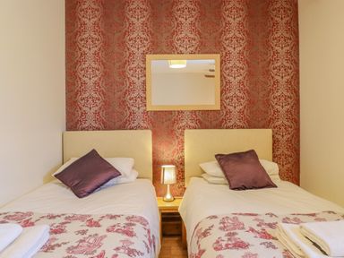 A bedroom with two single beds a bedside table with a lamp and a wall mirror at Hayloft Cottage in Little Glemham near Wickham Market