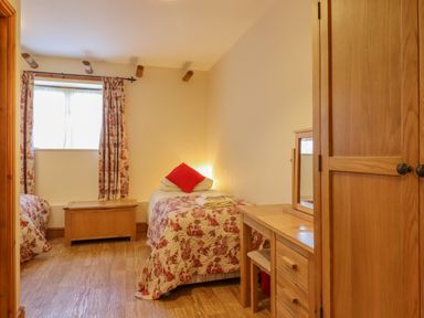 A bedroom with two single beds a wooden chest a wooden wardrobe and a wooden dressing table with a mirror at Hayloft Cottage in Little Glemham near Wickham Market