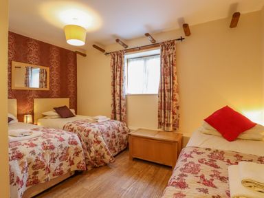 A bedroom with three single beds two on the left and one on the right with patterned bedspreads a window with curtains and a wooden chest under it at Hayloft Cottage in Little Glemham near Wickham Market
