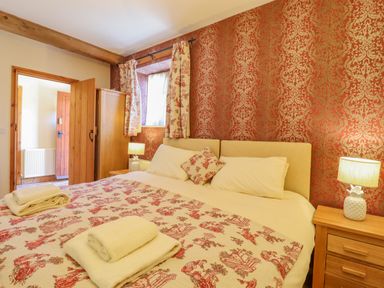A bedroom with a large bed bedside tables lamps and patterned wallpaper at Hayloft Cottage in Little Glemham near Wickham Market