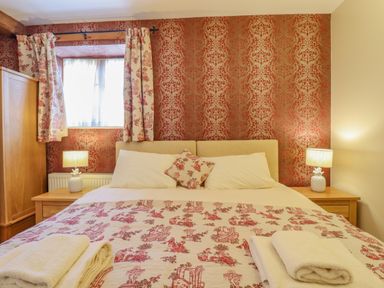 A bedroom with a patterned quilt on a bed two bedside tables with lamps and a window with curtains at Hayloft Cottage in Little Glemham near Wickham Market