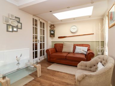 A living room with a brown leather sofa two pillows a beige armchair a glass coffee table and a wooden oar on the wall at Enfield in Porlock