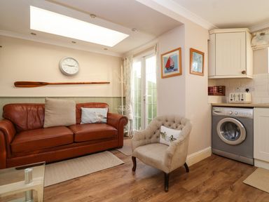 A living room with a brown leather sofa, beige armchair, clock on wall, washing machine, and glass door at Enfield in Porlock