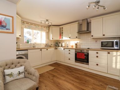 A kitchen with white cabinets wooden handles a washing machine microwave and an upholstered chair at Enfield Porlock