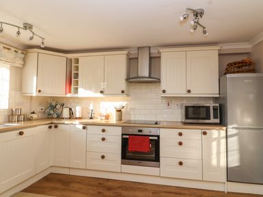 A kitchen with white cabinets wooden handles a microwave a refrigerator and an oven at Enfield in Porlock