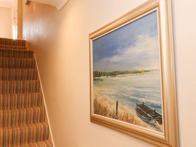 A staircase with striped carpet and a framed painting of a seaside scene on the wall at Enfield in Porlock