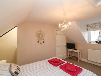 A bedroom with a bed with folded red towels a small table with a television a window and a door at Enfield in Porlock