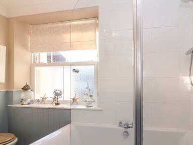 A bathroom with a bathtub shower and window sill decorated with seashells starfish a crab figure and a model sailboat at Enfield in Porlock