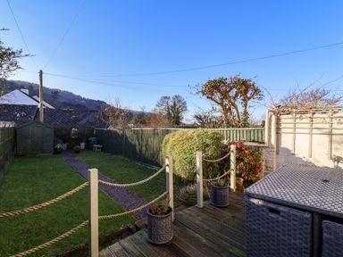 A backyard garden with a wooden shed a gravel path green grass and patio furniture at Enfield in Porlock