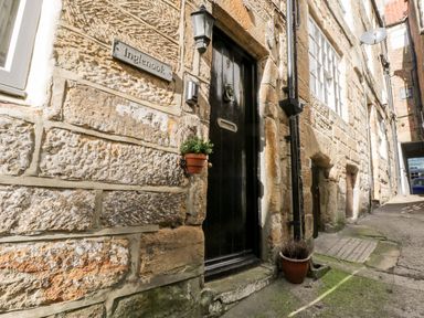 A stone building with a black door and a sign saying Inglennook on the wall at Inglenook Cottage in Whitby