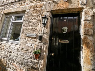 A black front door with the number 9 and a metal door knocker on a stone wall next to a window and a small plant at Inglenook Cottage in Whitby