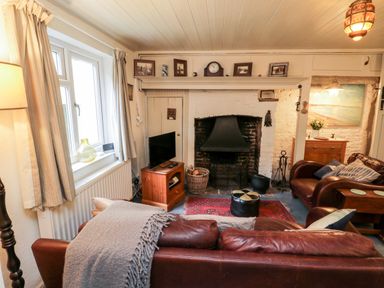 A living room with leather sofas a fireplace and a television at Inglenook Cottage in Whitby