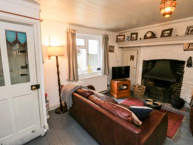 A living room with a brown leather sofa a floor lamp a window a television on a wooden stand and a fireplace at Inglenook Cottage in Whitby