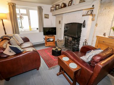 A living room with leather sofas a television a fireplace and a red rug at Inglenook Cottage in Whitby