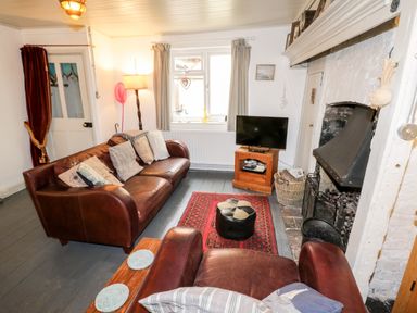 A living room with leather sofas a television a fireplace and a red rug at Inglenook Cottage in Whitby