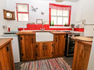 A kitchen with wooden cabinets red tiled backsplash farmhouse sink stove and colorful rug at Inglenook Cottage in Whitby