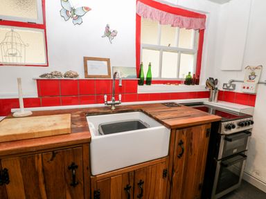 A kitchen with a white sink wooden cabinets red tiled backsplash and a stove at Inglenook Cottage in Whitby