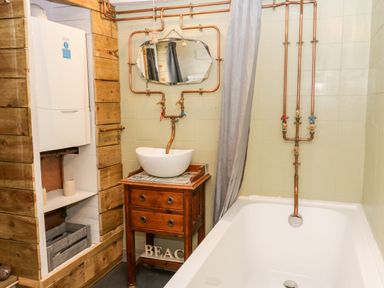 A bathroom with a bathtub wooden vanity with a bowl sink copper plumbing and a water heater at Inglenook Cottage in Whitby