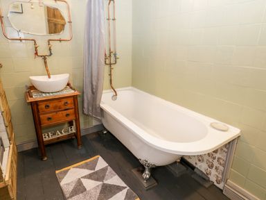 A bathroom with a clawfoot bathtub a wooden vanity with a basin sink a mirror and a geometric rug at Inglenook Cottage in Whitby