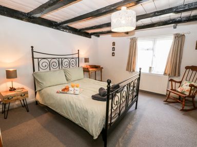 A bedroom with a metal bed frame a wooden rocking chair and a small wooden desk at Inglenook Cottage in Whitby