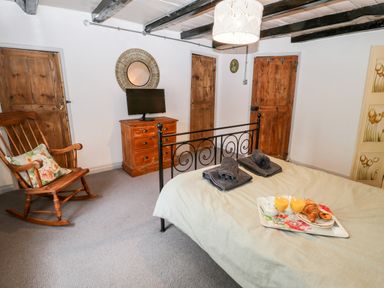 A bedroom with a bed a rocking chair a chest of drawers and a TV at Inglenook Cottage Whitby