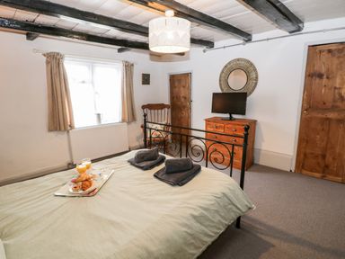 A bedroom with a bed with towels and breakfast tray a wooden dresser with a TV a wooden chair and two doors at Inglenook Cottage in Whitby