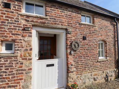 A brick building facade with a half white door and windows at The Bothy Lowick near Holy Island