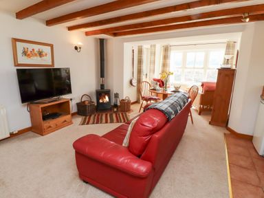 A living room with a red leather sofa a wood burning stove a television and a dining area with a round table at The Bothy in Lowick near Holy Island