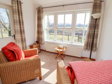 A sitting room with wicker armchairs red cushions small wooden side tables and windows with beige plaid curtains at The Bothy Lowick near Holy Island