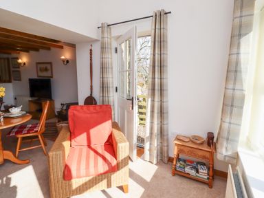 A living room with a red cushioned armchair near a door with plaid curtains and a small wooden table with books at The Bothy in Lowick near Holy Island