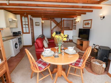 A living area with a round dining table set for two with daffodils in a vase a red sofa kitchen appliances and a television with wooden beams on the ceiling at The Bothy Lowick near Holy Island