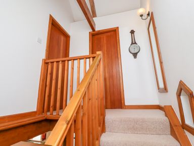 A staircase with wooden railings carpeted steps two wooden doors a wall clock and two mirrors at The Bothy in Lowick near Holy Island