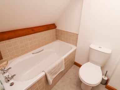 A bathroom with a bathtub tiled with beige squares and a white toilet at The Bothy in Lowick near Holy Island