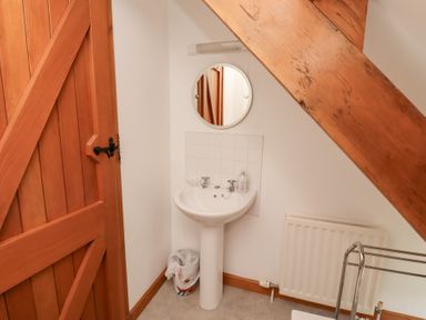 A small bathroom with a wooden door a round mirror a pedestal sink and a radiator under a wooden beam at The Bothy in Lowick near Holy Island