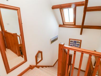 A staircase with wooden railings a mirror on the wall skylight window and framed pictures at The Bothy in Lowick near Holy Island
