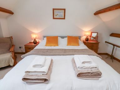 A bedroom with a double bed towels on the bed bedside tables with lamps and a chair at The Bothy in Lowick near Holy Island
