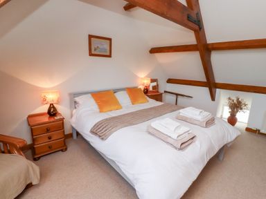 A bedroom with a bed with yellow pillows and folded towels on it two wooden bedside tables with lamps wooden ceiling beams and a small framed picture on the wall at The Bothy in Lowick near Holy Island