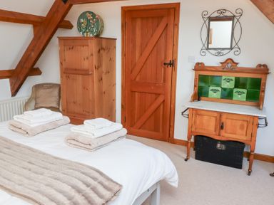 A bedroom with a bed folded towels a wooden wardrobe a wooden door a chair a wooden cabinet with green tiles and a mirror at The Bothy in Lowick near Holy Island