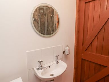 A small bathroom sink with two taps a round mirror above and a mounted soap dispenser next to a wooden door at The Bothy in Lowick near Holy Island