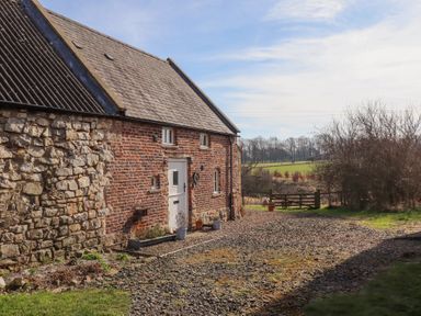 A rustic brick and stone building with a gravel driveway and a wooden gate in a rural setting at The Bothy in Lowick near Holy Island