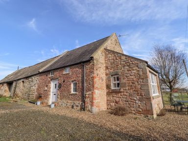 A stone and brick cottage with a white door and windows with a gravel yard and outdoor table and chairs at The Bothy in Lowick near Holy Island