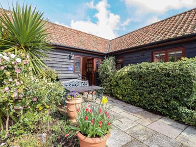 A patio with potted plants a bench and a table outside a building with tiled roof at Poppy Cottage in Little Glemham near Wickham Market