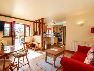 A living room and kitchen with wooden furniture and red sofa at Poppy Cottage in Little Glemham near Wickham Market