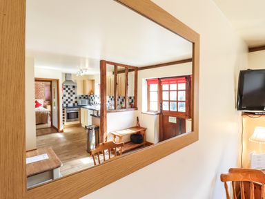 A reflection of a kitchen and entrance door with wooden bench and a dining table with chairs at Poppy Cottage in Little Glemham near Wickham Market
