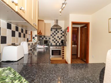 A kitchen with black and beige checkered tiles a toaster kettle microwave oven and wooden cabinets at Poppy Cottage in Little Glemham near Wickham Market