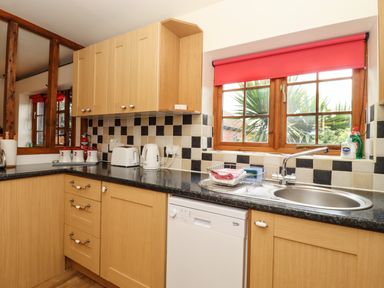 A kitchen with wooden cabinets a black countertop a dishwasher a sink and a window with a red blind at Poppy Cottage Little Glemham near Wickham Market