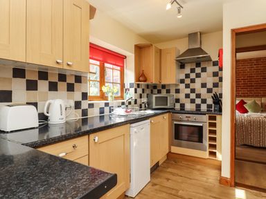 A kitchen with wooden cabinets black and beige checkered backsplash and appliances at Poppy Cottage in Little Glemham near Wickham Market